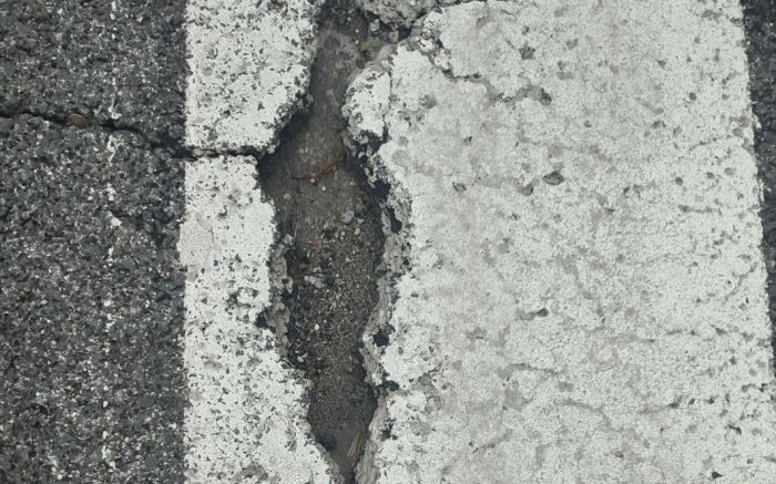 Crepa e buca sulle strisce pedonali davanti alla scuola Saba: pericolo per pedoni e motocicli